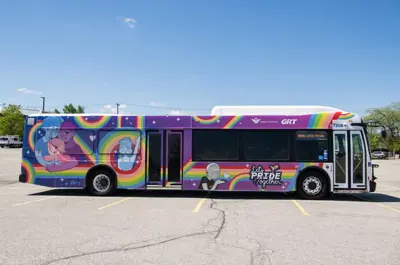 conventional bus wrapped in a colourful Pride design parked in an empty parking lot