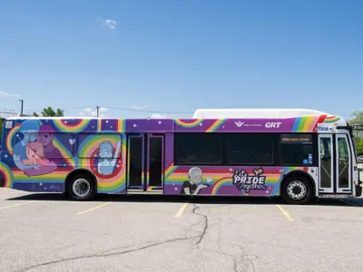 conventional bus wrapped in a colourful Pride design parked in an empty parking lot