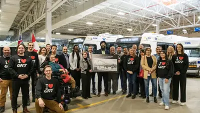 group of people standing in a bus garage in front of three buses