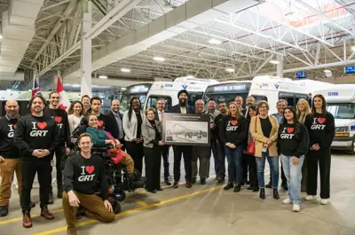 group of people standing in a bus garage in front of three buses