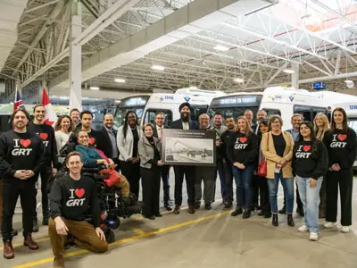 group of people standing in a bus garage in front of three buses